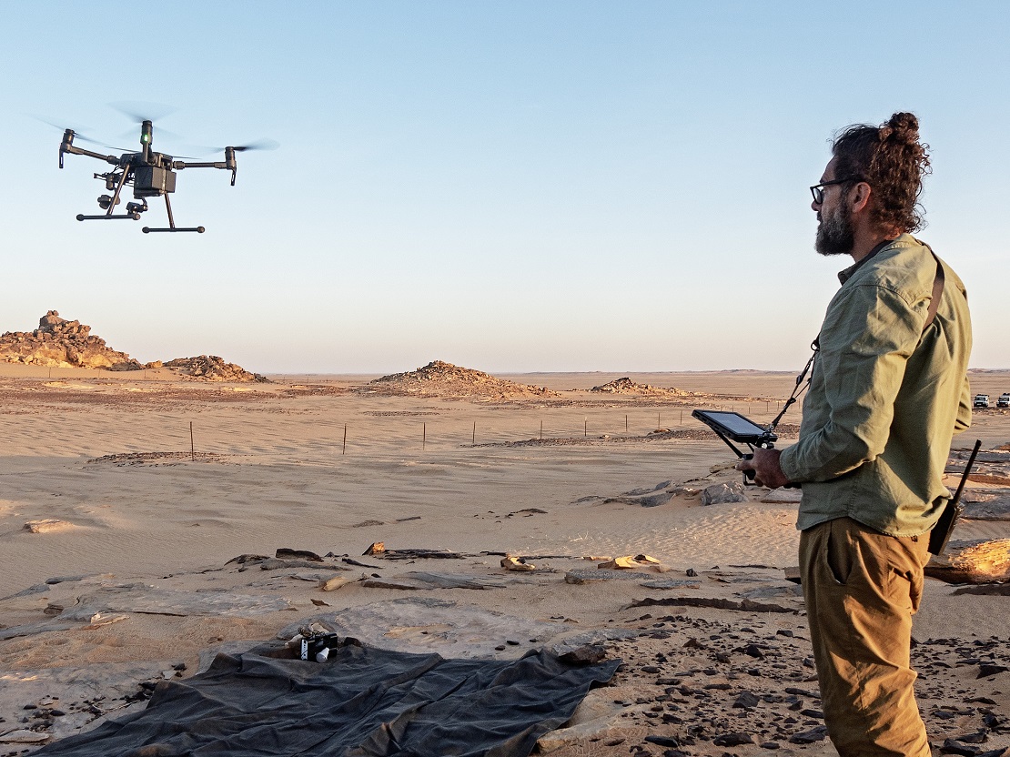 Een man van in de dertig leidt een drone over een woestijnoppervlak in Tsjaad...