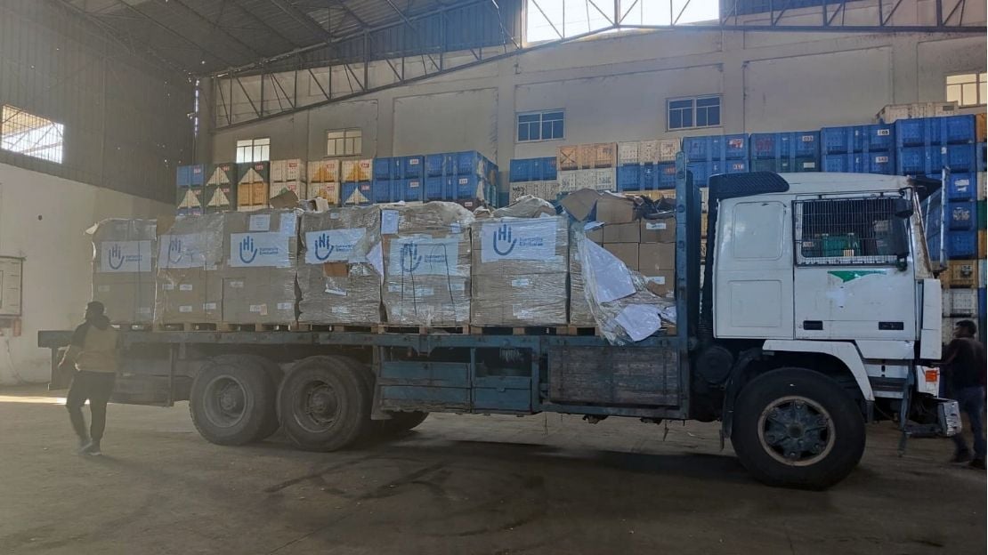 Un camion chargé de cartons portant le logo de Handicap International se trouve dans un hangar.