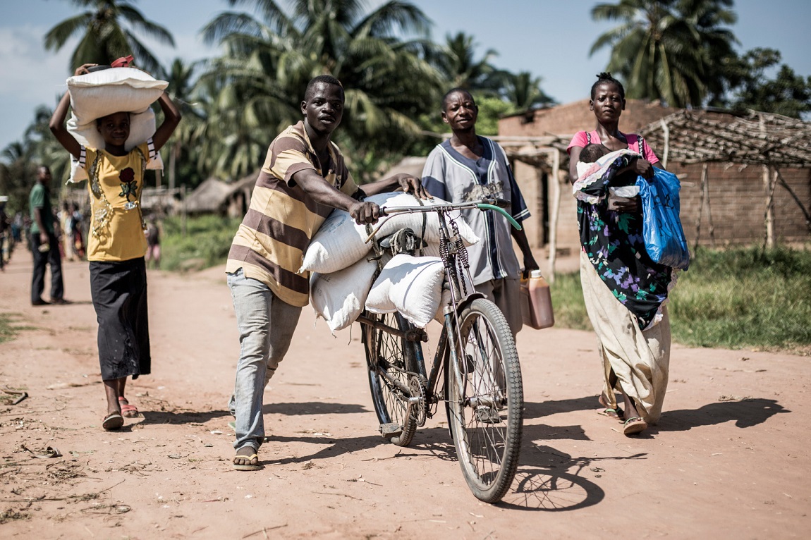 Twee Congolezen duwen een fiets met zakken die door Handicap International en Food for Peace werden verdeeld. Een vrouw draagt een tas op haar hoofd terwijl een andere vrouw een kind naast zich draagt.