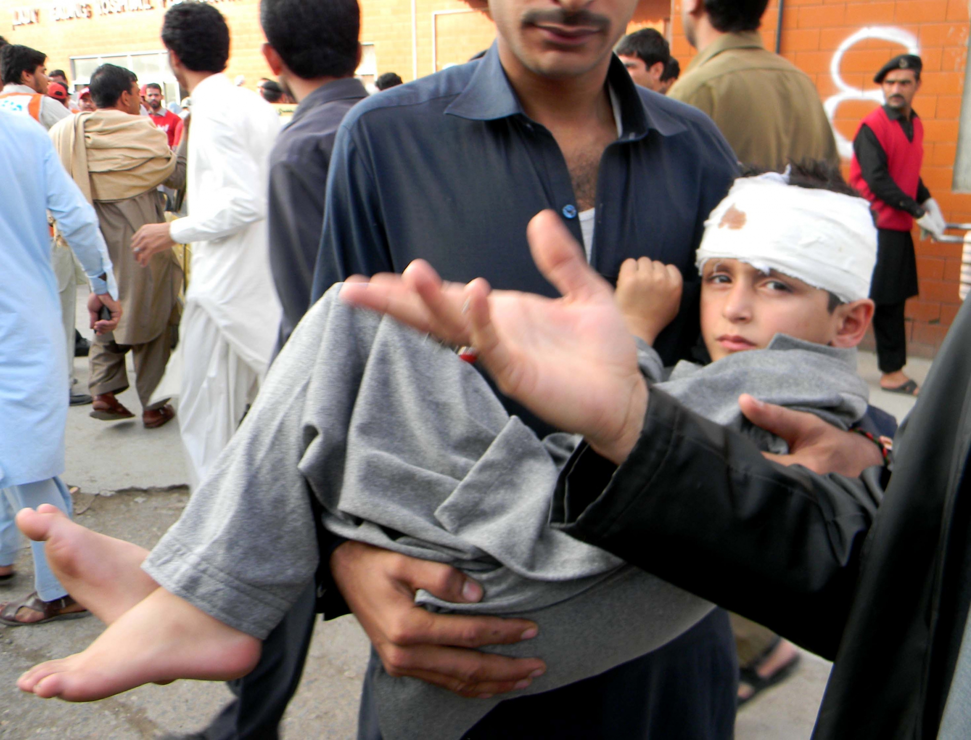 Un homme porte un jeune garçon dans ses bras. L'enfant à la tête bandée.