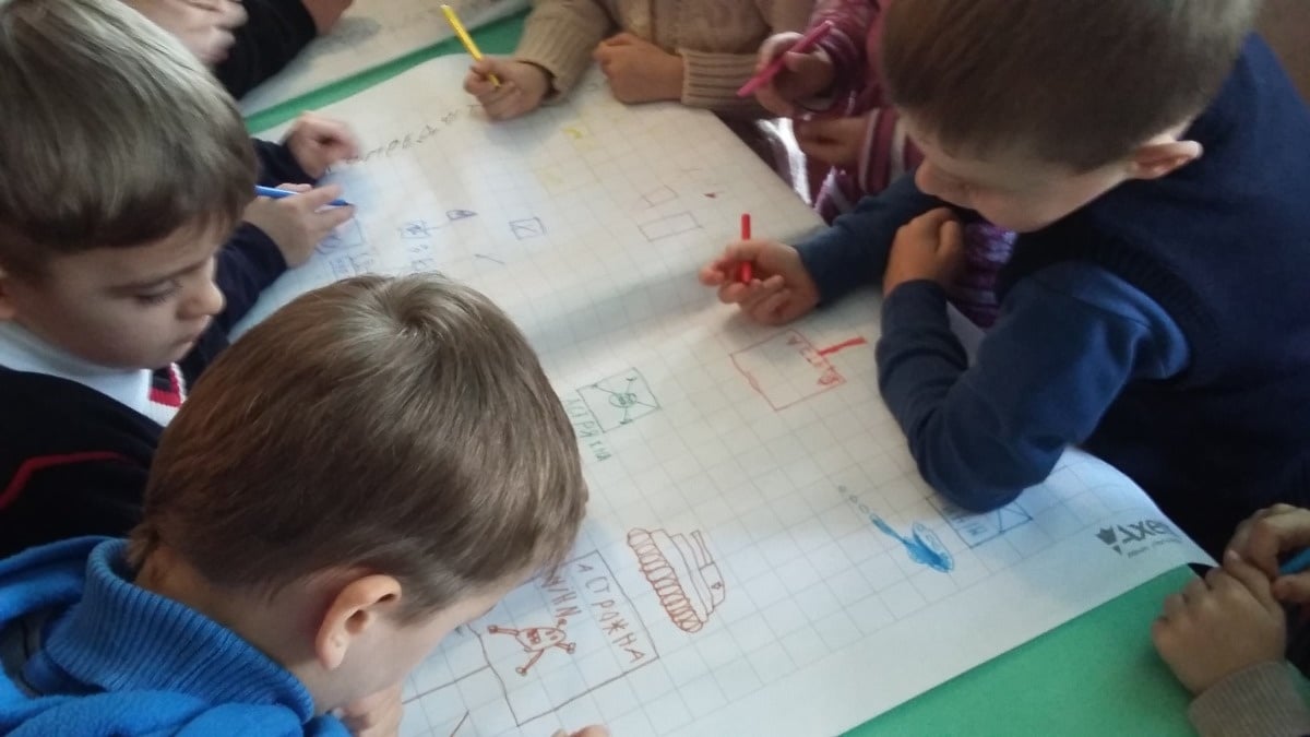 Een viertal kinderen dat rond een tafel zit, buigt zich over hun tekeningen die ze maken over mijnen