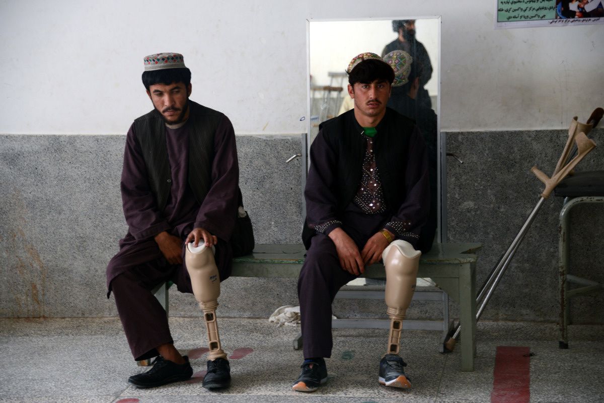 deux jeumes hommes afghans assis sur un ban. La jambe gauche de leur pantalon est relevée et montre leur prothèse pas encore terminée : on voit encore la structure en métal.