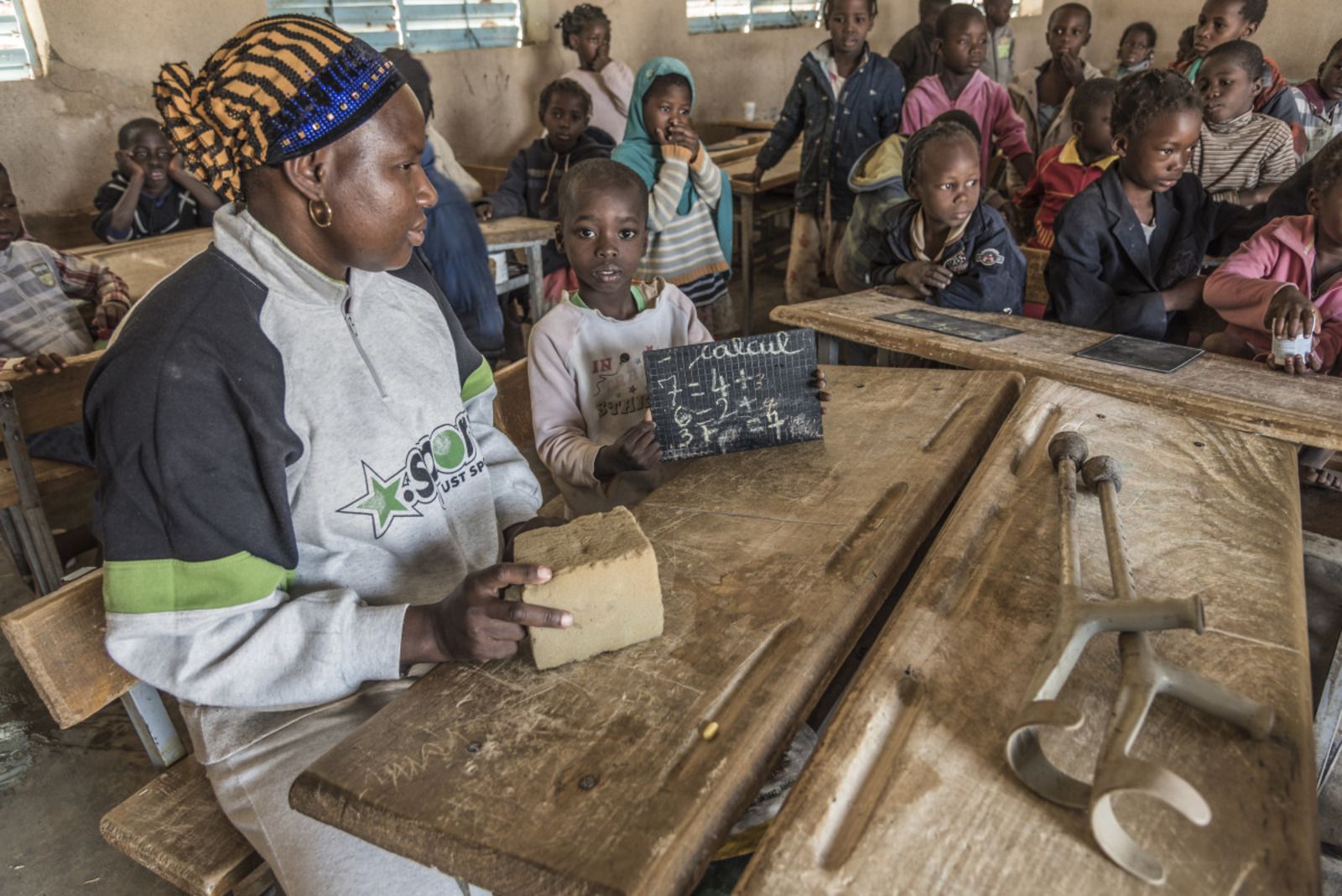 Samadou op school : hij toont zijn schrijflei met rekensommen. De vliegende leerkracht zit naast hem.