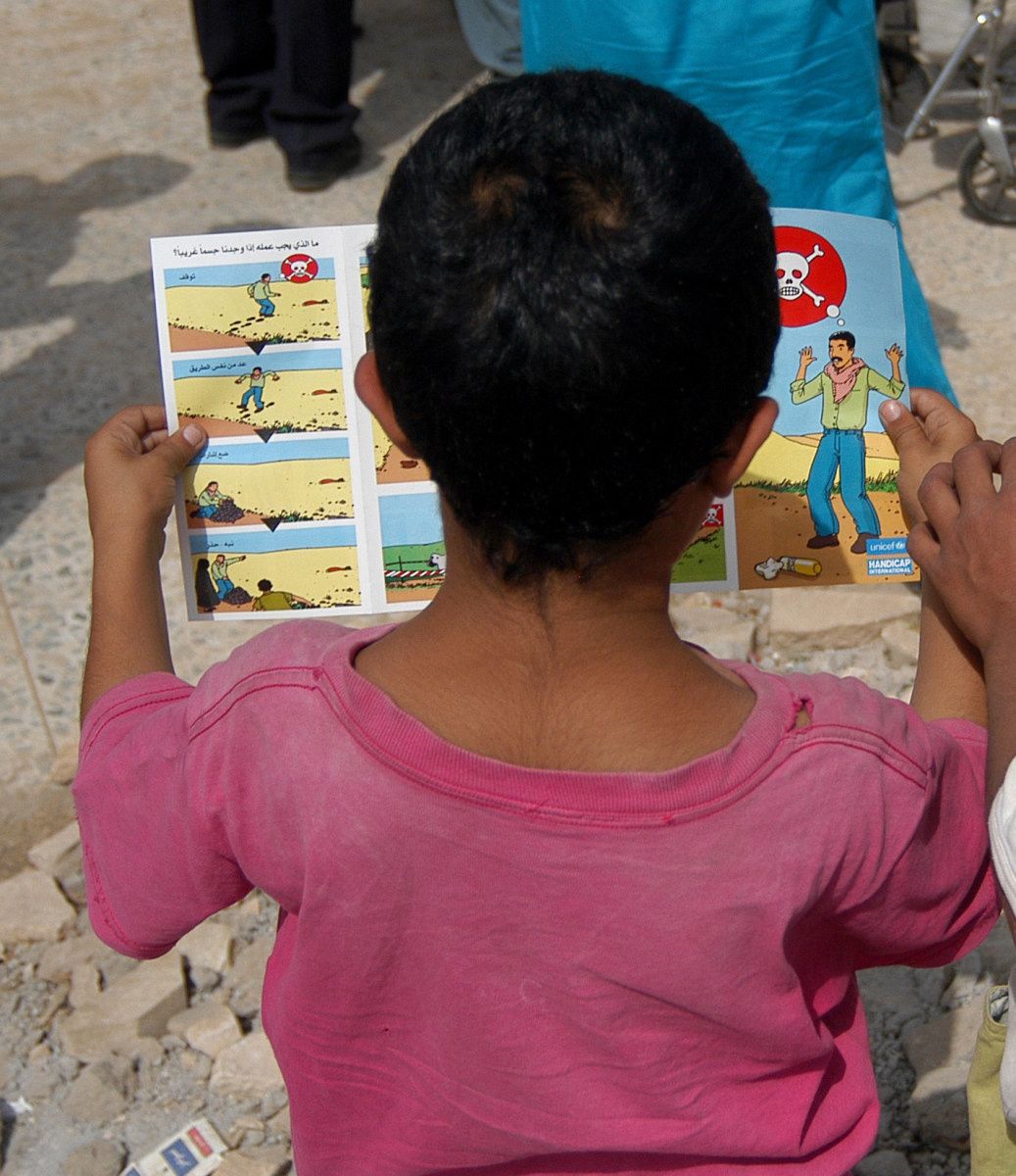 Un enfant regarde une brochure de sensibilisation aux dangers des mines