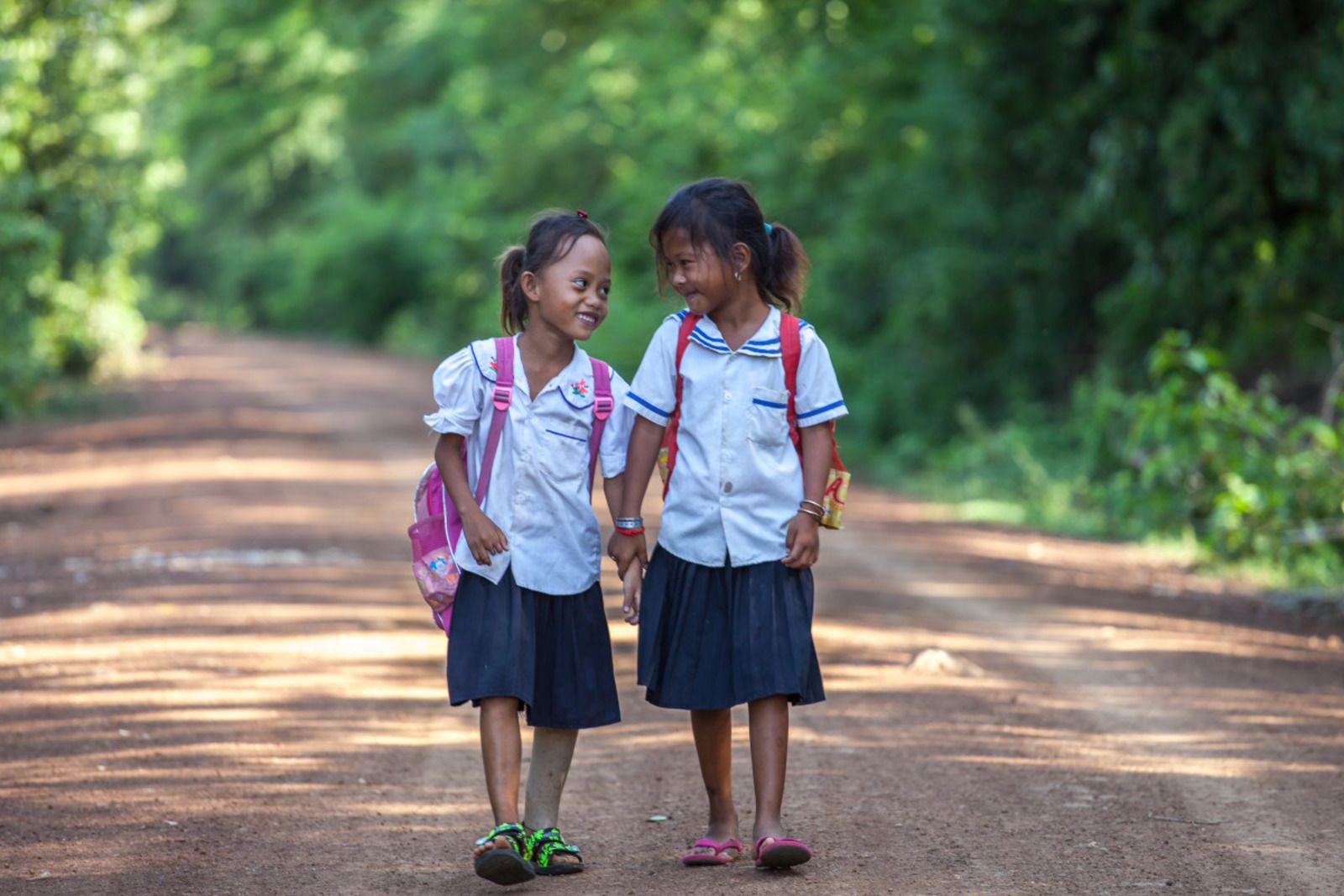 Channa en een vriendin - allebei in schooluniform: wit hemd en blauwe rok – lopen over een aardeweg naar school.