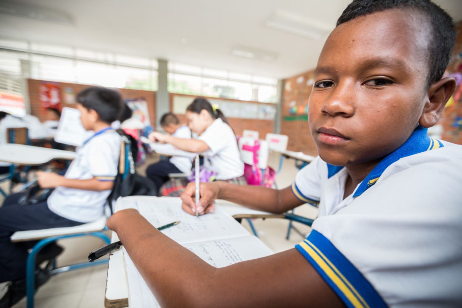 Jemerson, een jonge Colombiaan van 13 jaar, zit in de klas met een schrift voor zich. Zijn linkerhand werd geamputeerd.