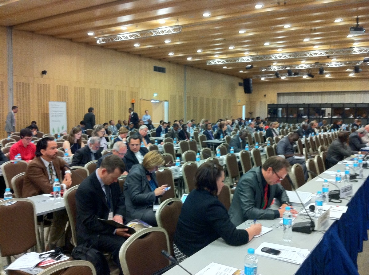 Volle conferentiezaal met lange tafels en afgevaardigden