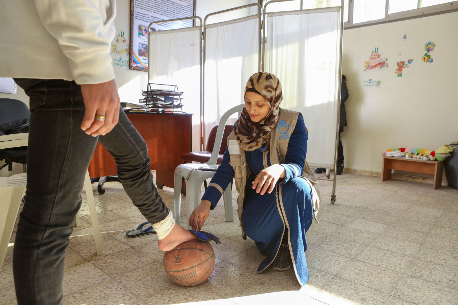 Een Palestijnse ergotherapeute plaats de voet van een jonge man op een bal voor een evenwichtoefening.