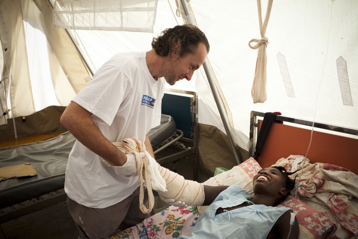 Olivier Champagne houdt de arm vast van een patiënt op een bed in een tentenhospitaal.