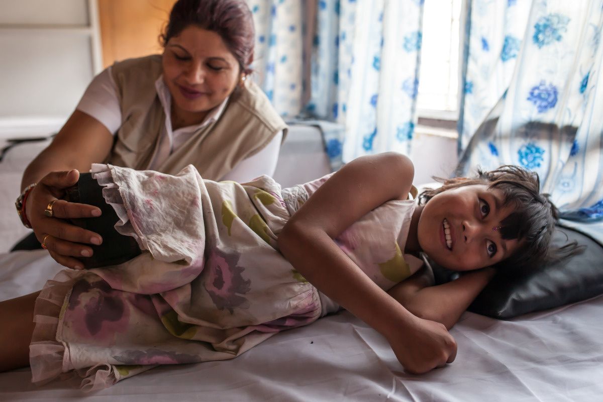 Nirmala, une petite fille de 9 ans, amputée de la jambe droite, allongée sur un lit. Elle fait un exercice sans sa prothèse avec une kiné de Handicap International