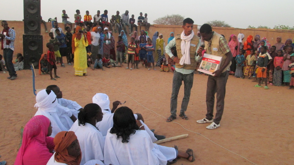 Twee animatoren van Handicap International tonen middenin een kring van toehoorders sensibiliseringsafbeeldingen 