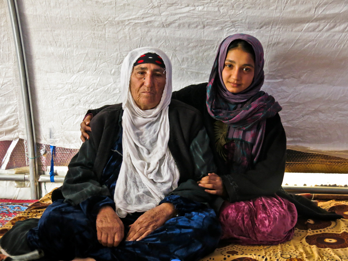 Portret van Reema en Dhoha, die haar oma teder vasthoudt, met het tentzeil op de achtergrond.