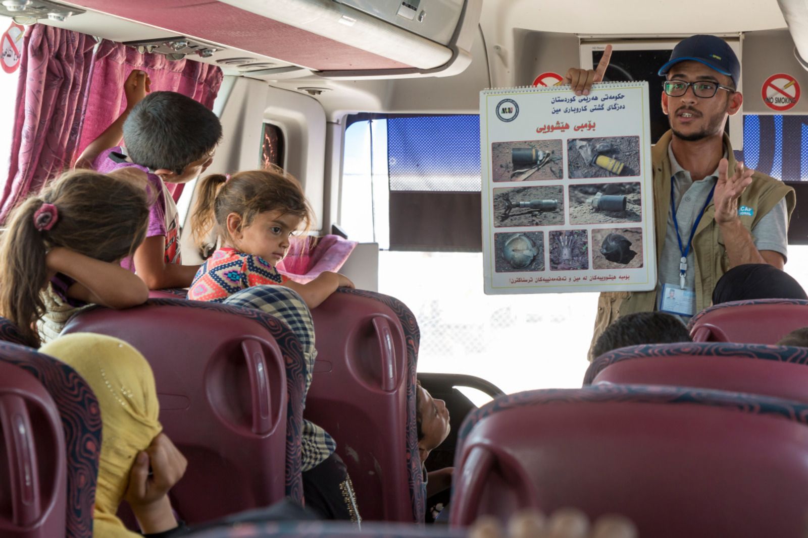 Un agent de sensibilisation de HI montre un poster avec des photos de mines à des personnes assises dans le bus qui doit les ramener à Mossoul