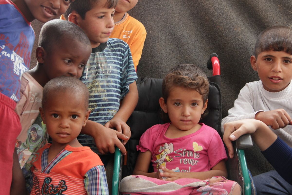 Een 4-jarig meisje in een rolstoel omringd door andere kinderen in een tent