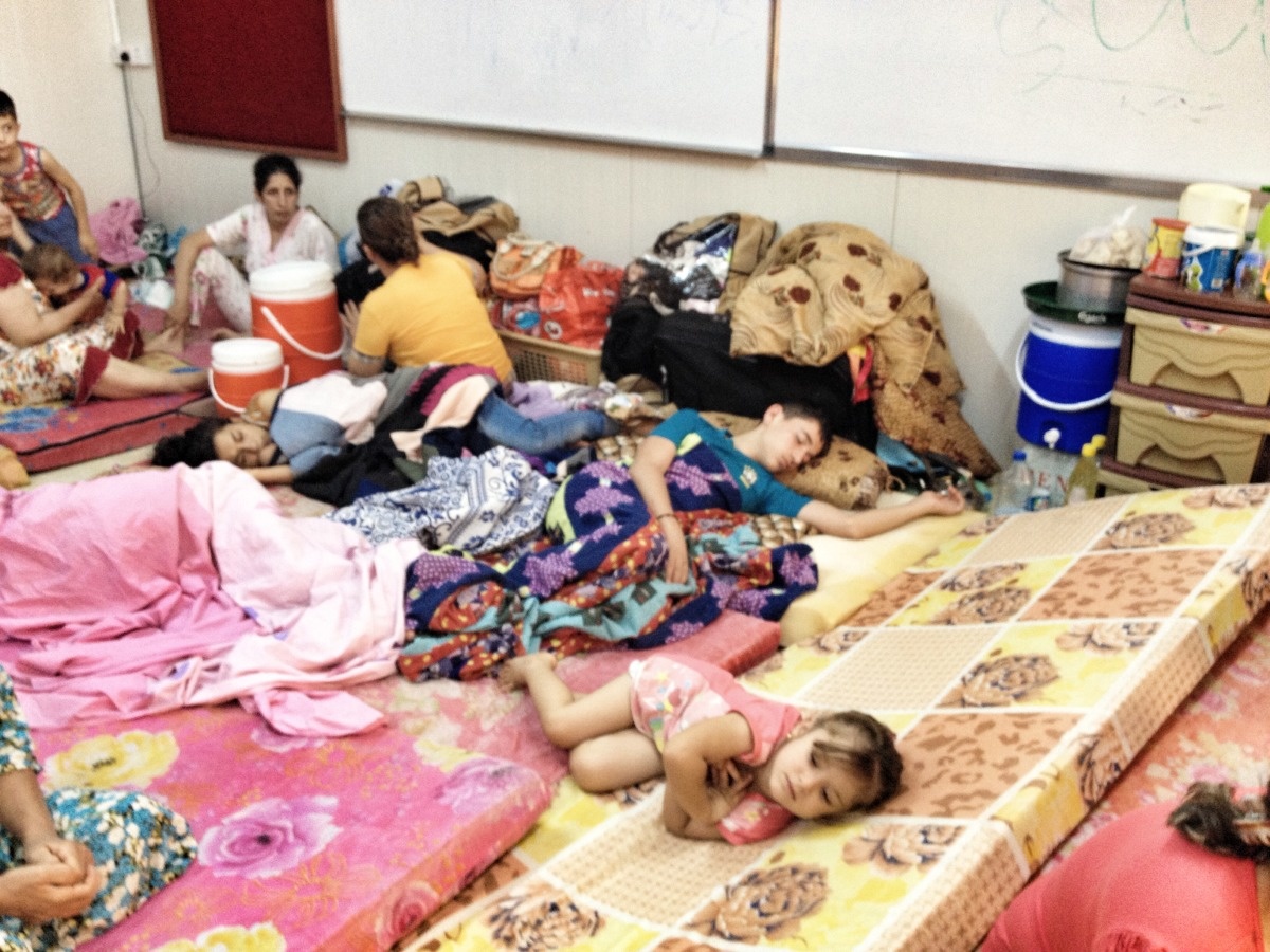 une maman et des enfants endormis sur des matelas dans un petit local de classe.