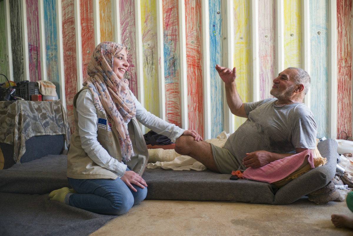 Een kinesiste van Handicap International houdt de stomp vast van een oude man op een matras in een kleurrijke ruimte.