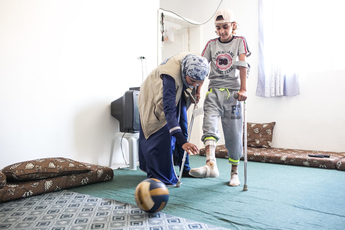 Een kinesiste van Handicap International doet een baloefening met een jongen die op krukken loopt en die ortheses draagt aan beide benen