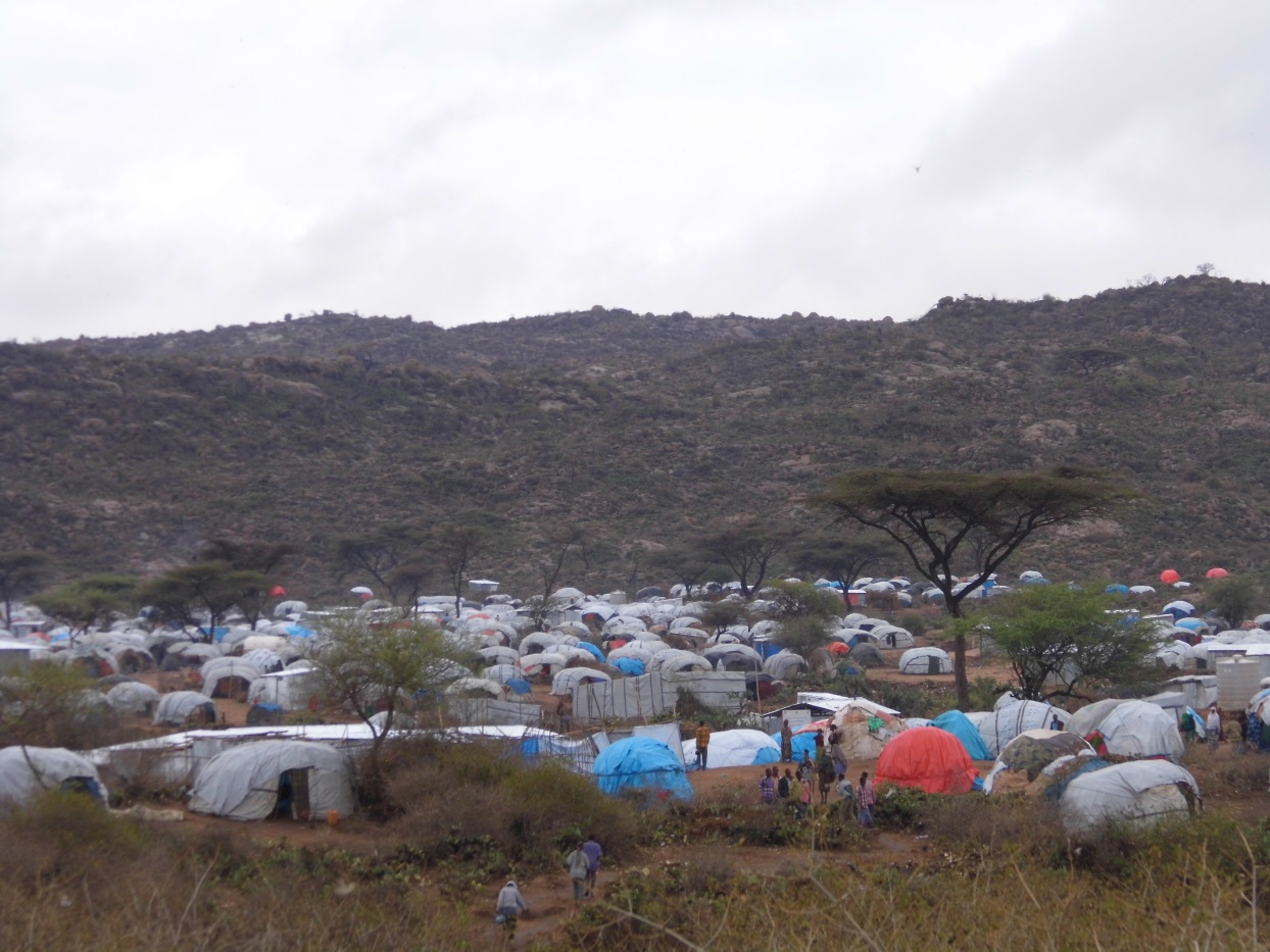 Een tentenkamp met tientallen tentjes en mensen die op paden ertussen lopen in een dal