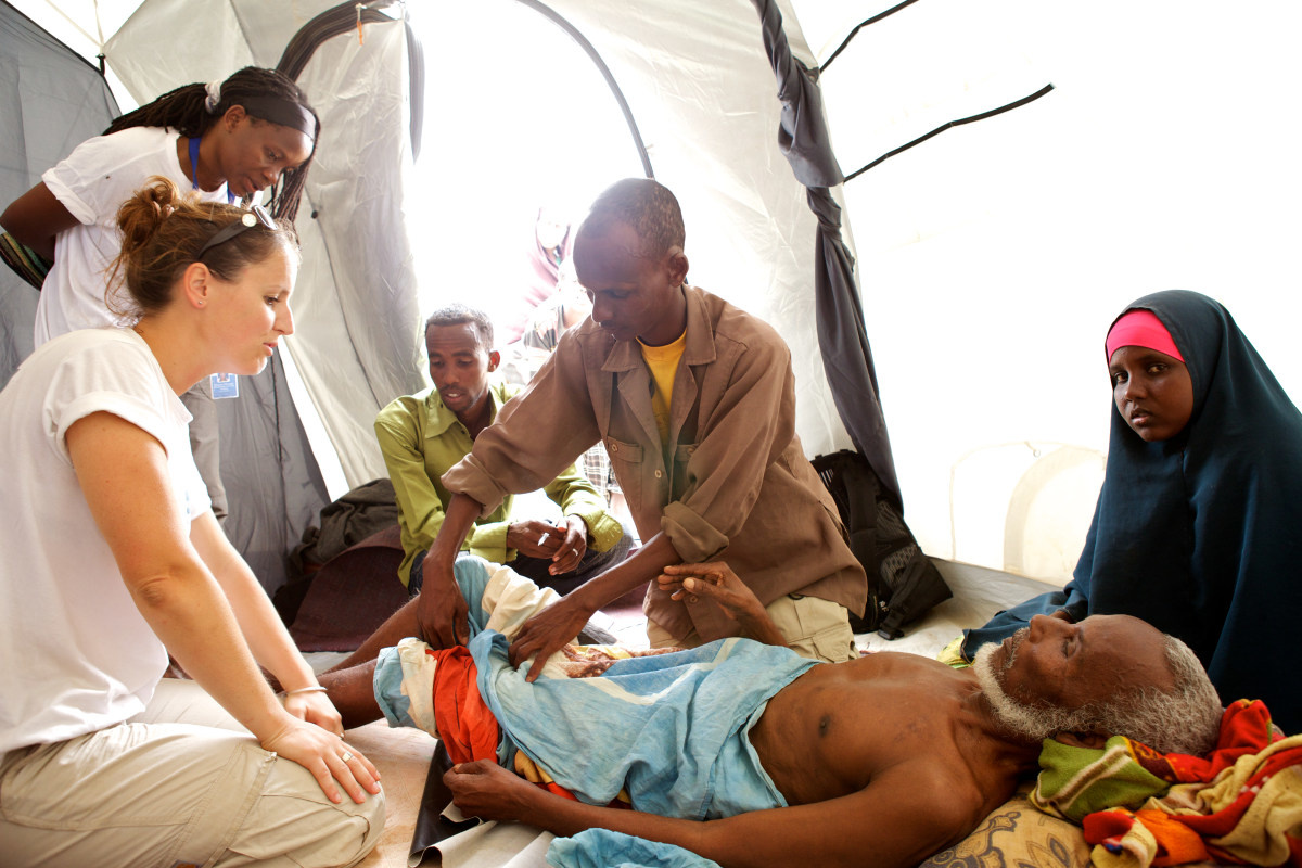 Drie medewerkers van Handicap International behandelen een oude man die in een tent ligt.