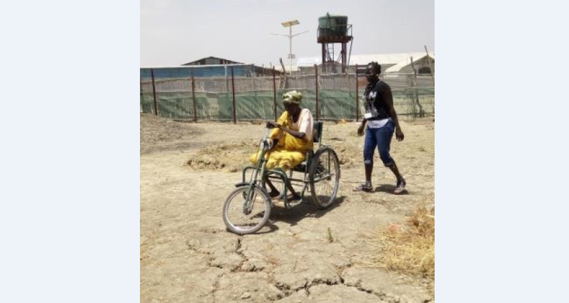 Mary op haar driewieler van Handicap International met een dame die achter haar aan stapt