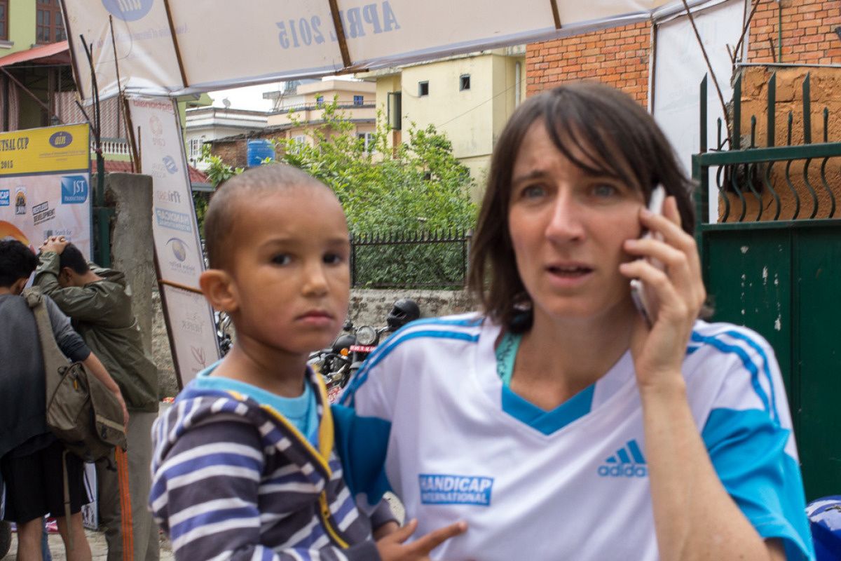 Een expat van Handicap International aan de telefoon met een kind op haar arm.