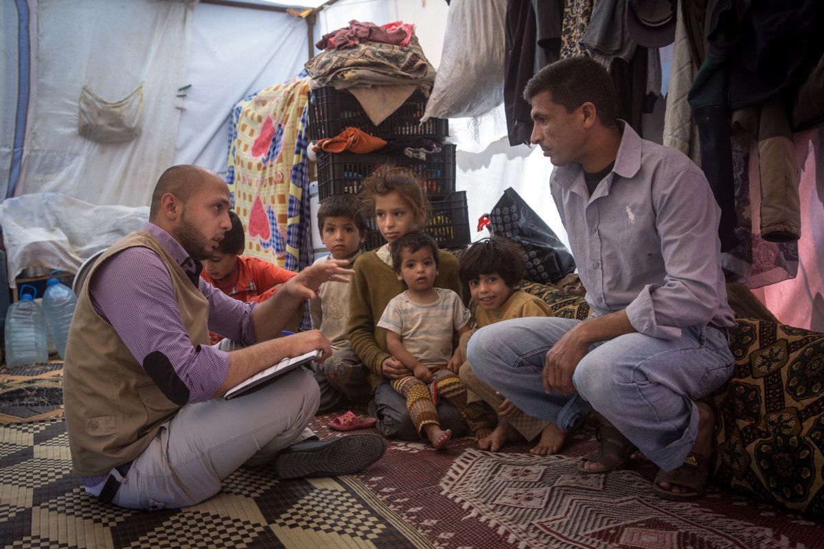 Een medewerker van Handicap International zit onder een tent. Hij praat met een man met 5 kinderen naast hem