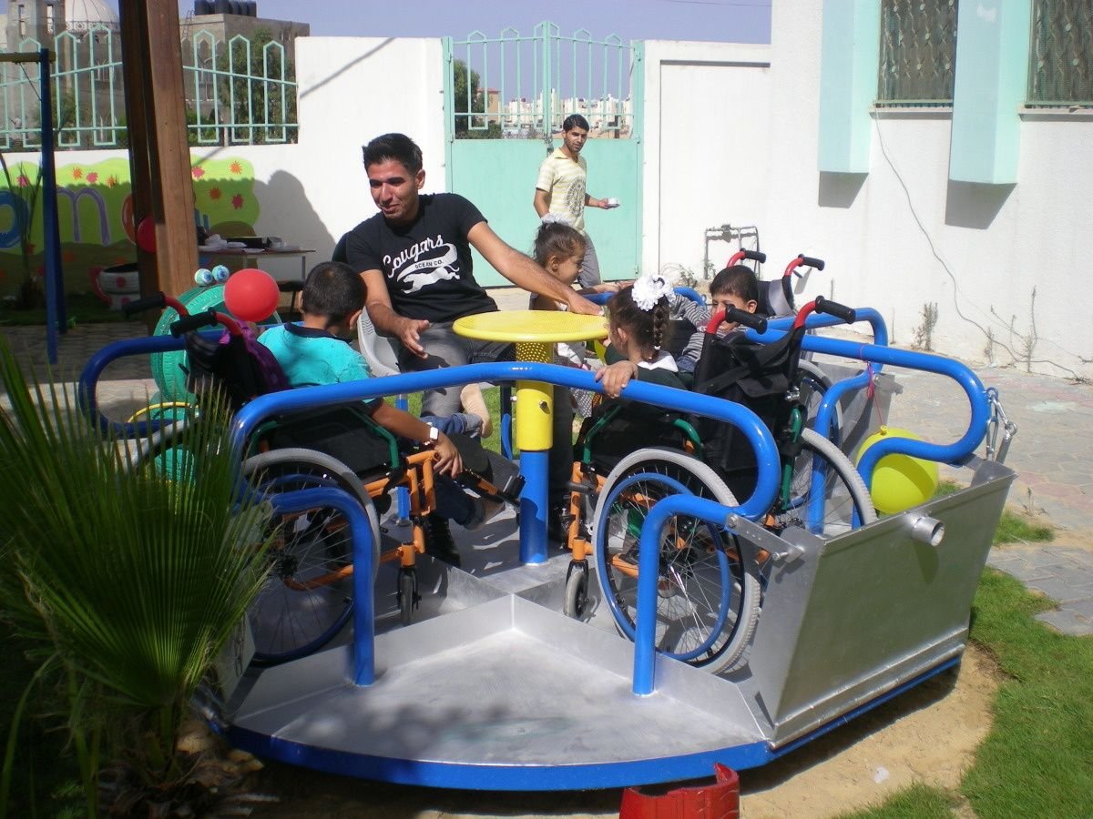 Des enfants en chaise roulante sur un tourniquet adapté, peint de couleurs vives