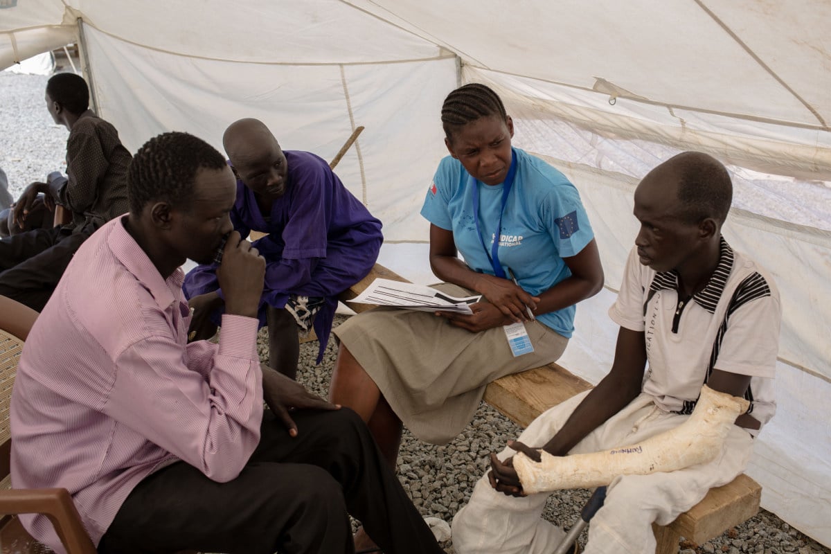 Man met arm in gips in tent in gesprek met mensen van Handicap International