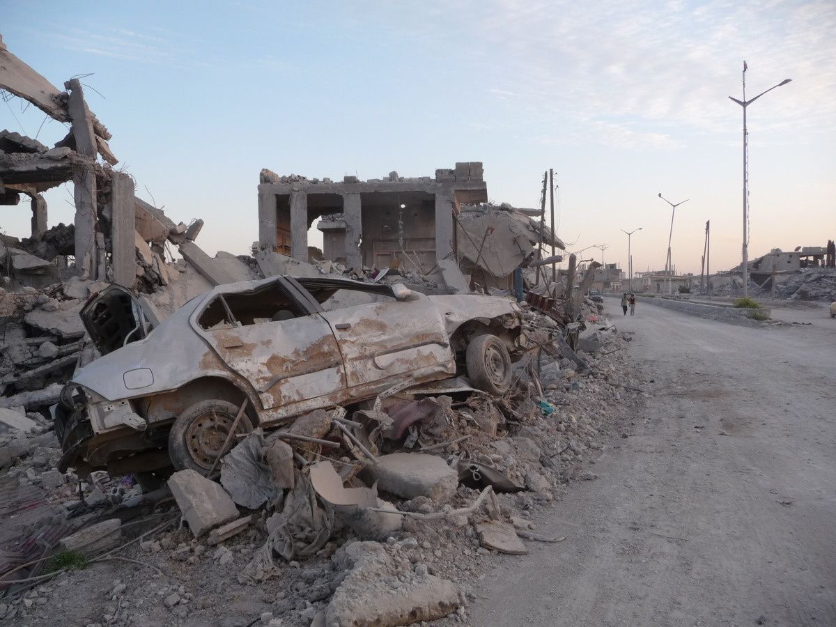 Stoffige en verlaten straat in Kobani met brokstukken langs de zijkant en een vernielde auto.