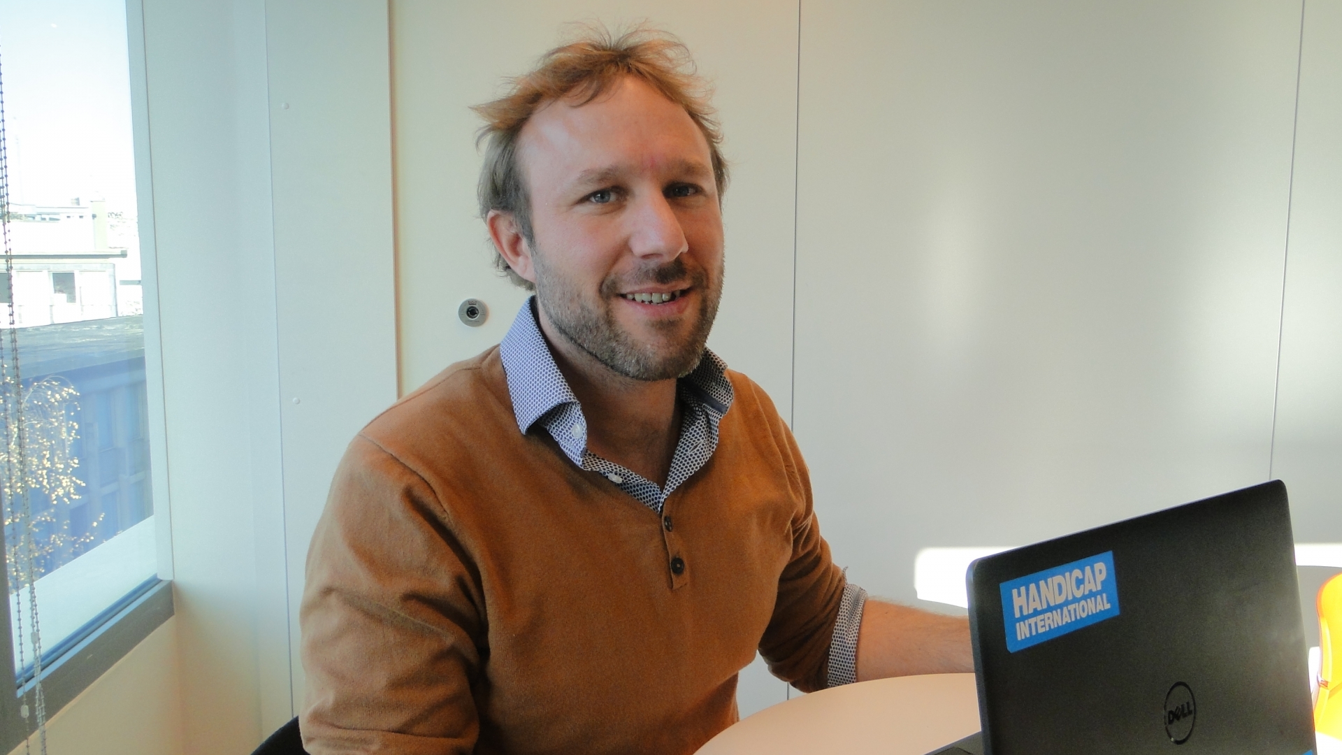 Portrait d'Arnaud Pont: homme d'une trentaine d'année aux cheveux blonds coupés court, une barbe de quelques jours, assis à une table derrière son ordinateur portable